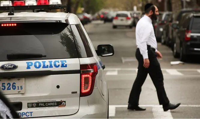 Hasidic man walks by a police car in a Orthodox Jewish neighborhood in Brooklyn
